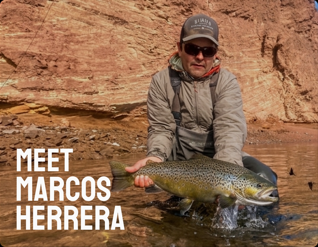 Marcos Herrera kneeling in the shallows with a brown trout