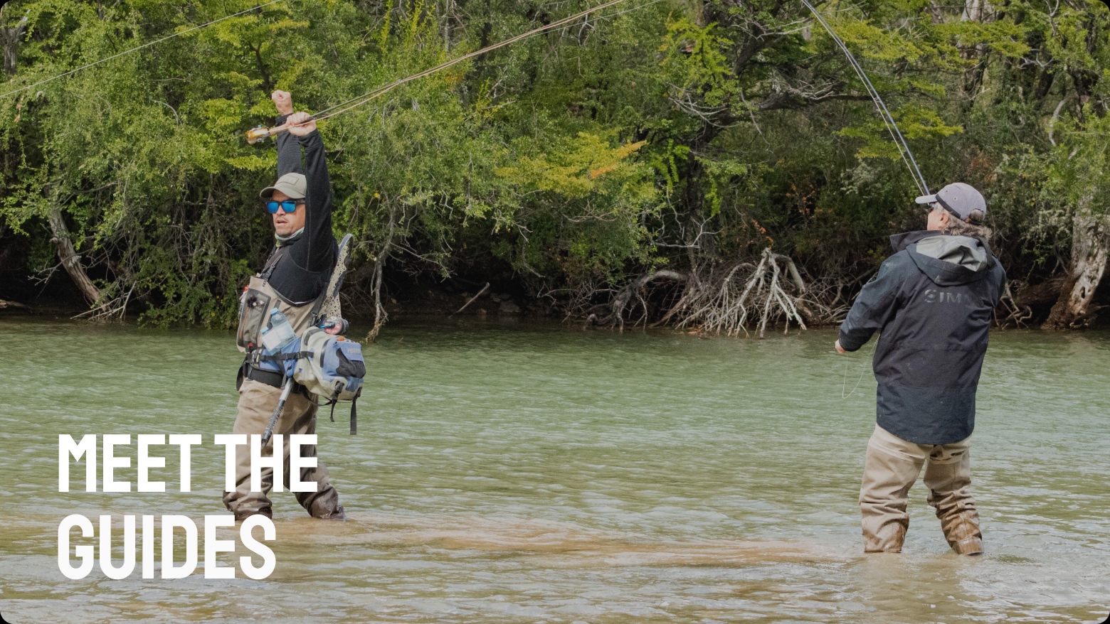 Two guides kneeling in the shallows holding a trout before release