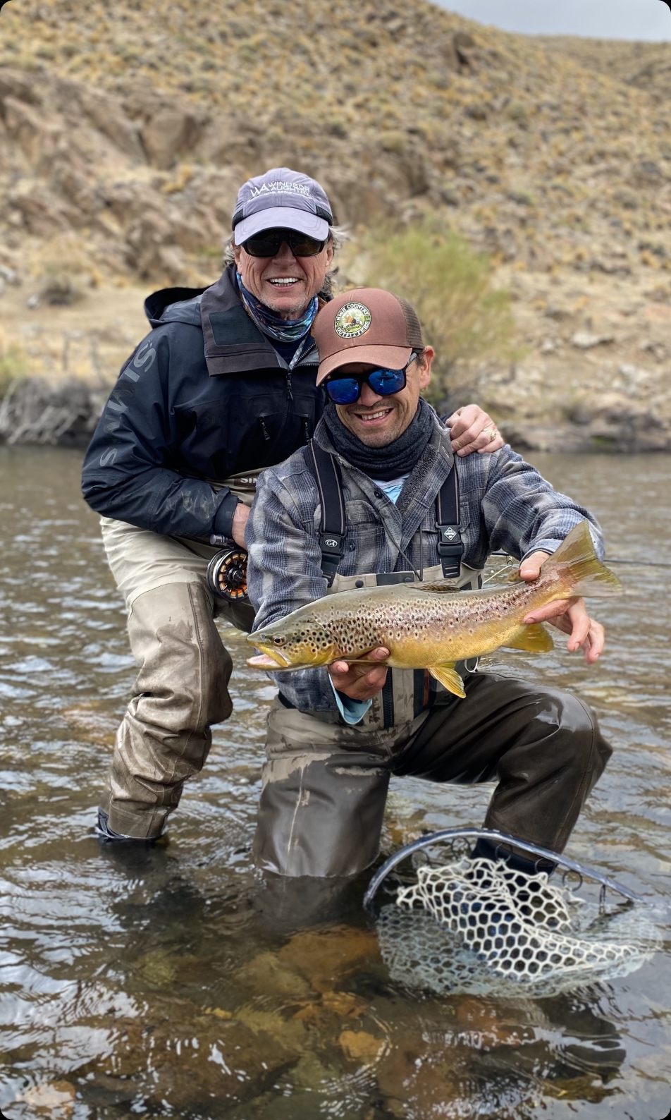 Anglers kneeling in the shallows with a brown trout